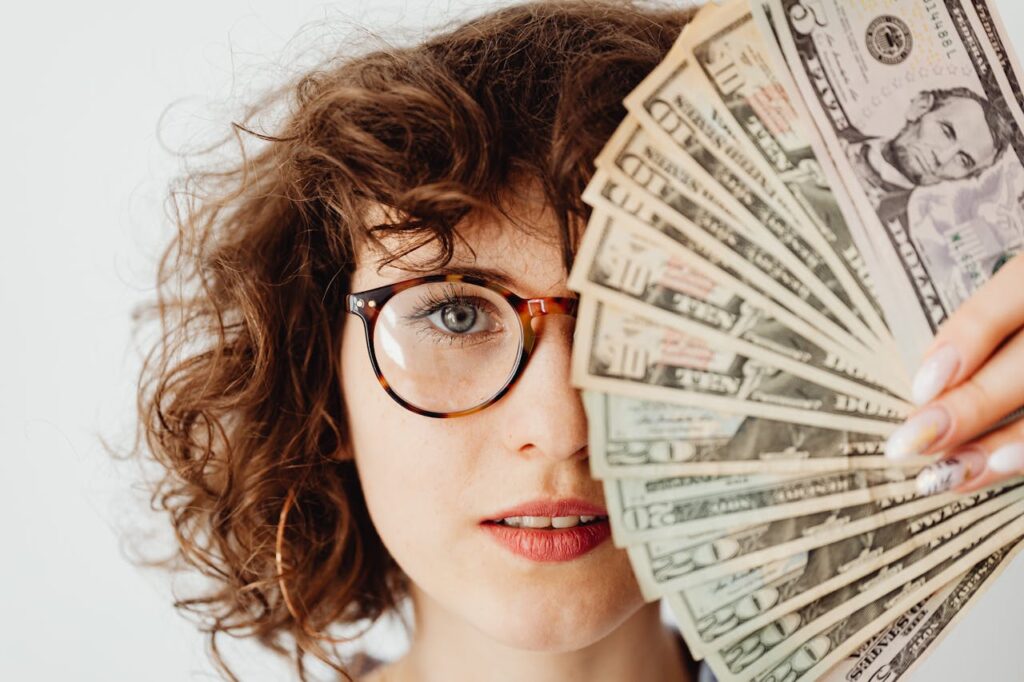 Caucasian woman with eyeglasses holding US dollar bills, highlighting finance and savings.